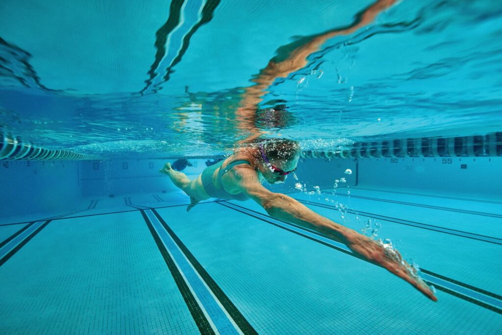 A woman swims underwater in a swimming pool, wearing goggles and a swimsuit.